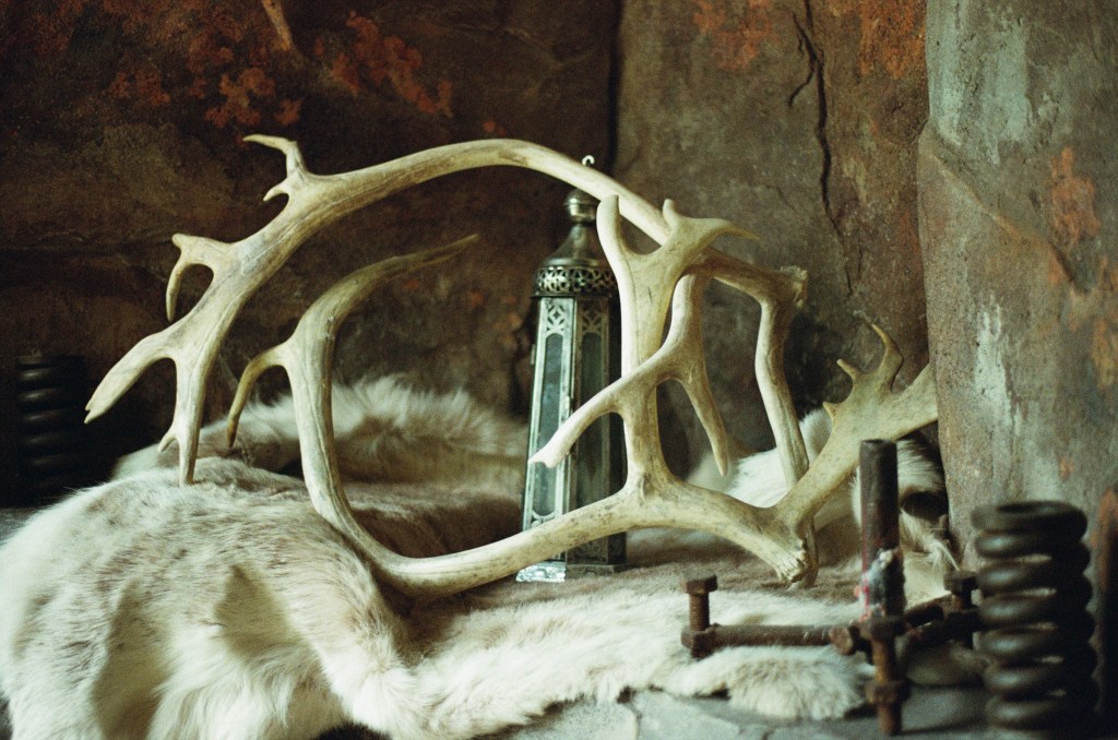 A reindeer hide is sitting on the side with artefacts of the mining town. On top of the hide is a lantern, unlit, with reindeer antlers. 