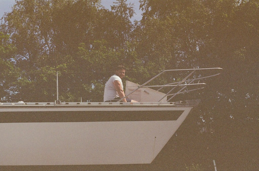 A man sits at the front of a yacht with a locker open.