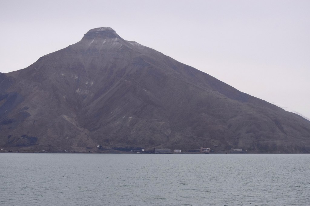 A pyramid shaped mountain is seen in the distance. Buildings are lining at the bottom of the mountains. 