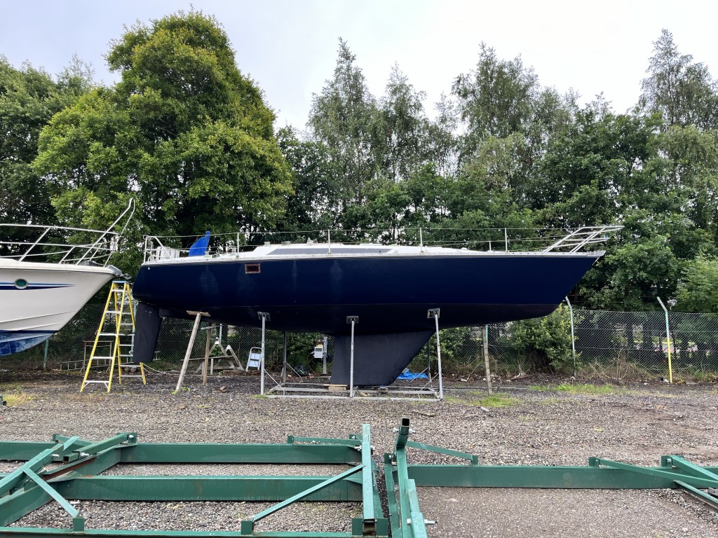 A side view of a dark blue boat with black antifoul in its cradle. 