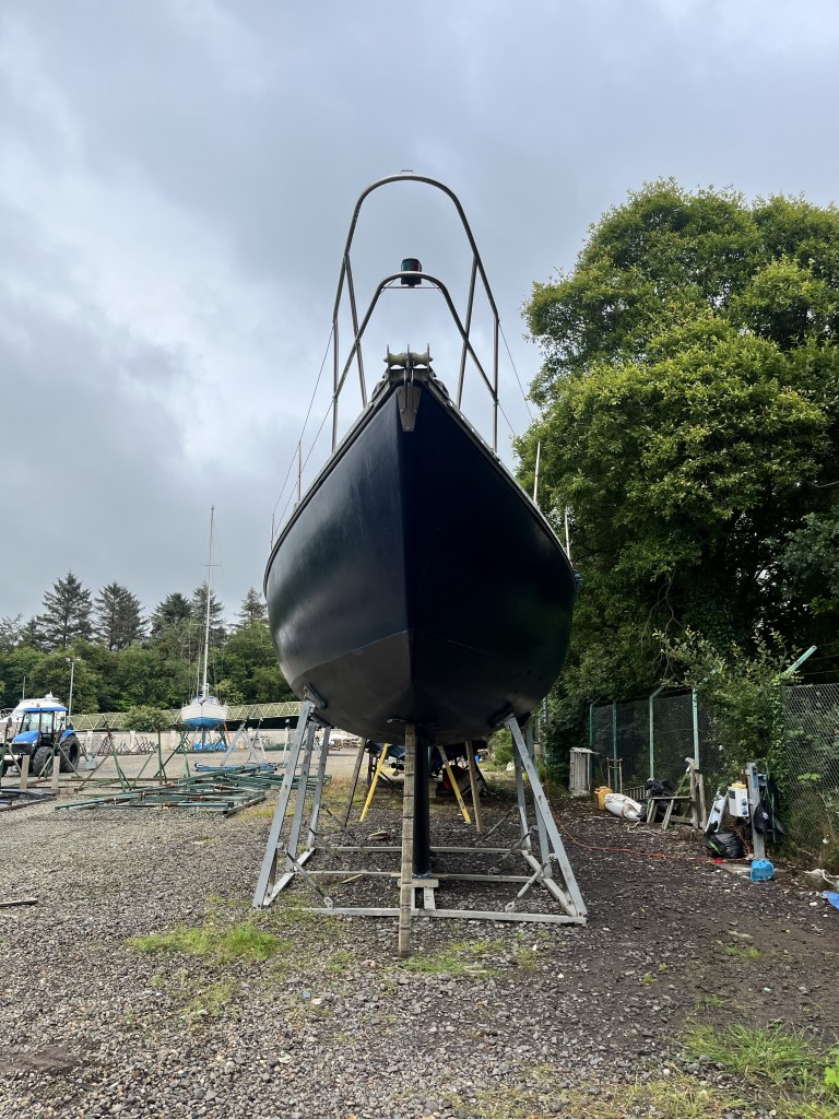A view from the front of the boat in the boat yard in its cradle shows a shiny dark blue hull and black antifoul 