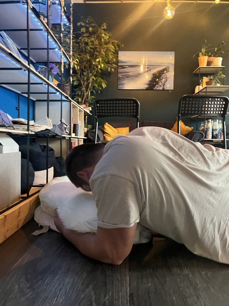 A man lays down on the floor, he is cuddling a white husky.