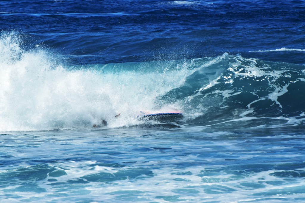 A wave with a down surfer, the water is blue.
