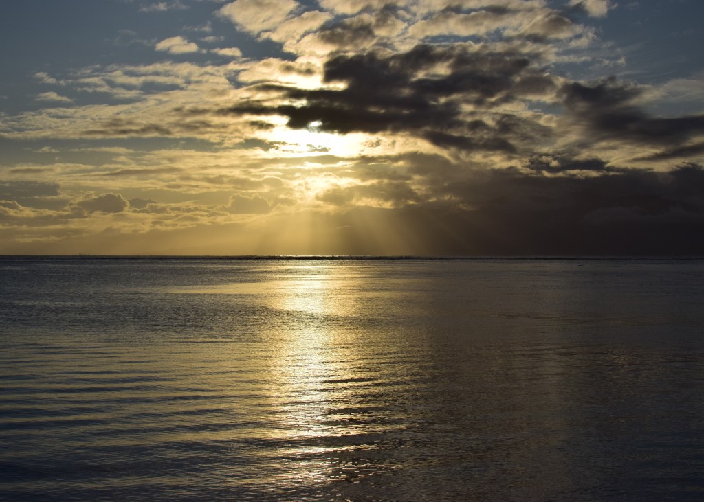 Sun beams cut through the clouds and the faint outline of an island can be seen.
