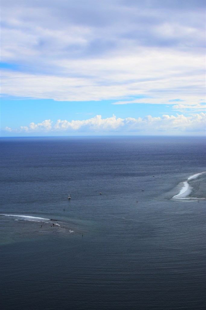 Seascape shows a break in the shallow line of sand around the island a boat is heading towards the opening. 