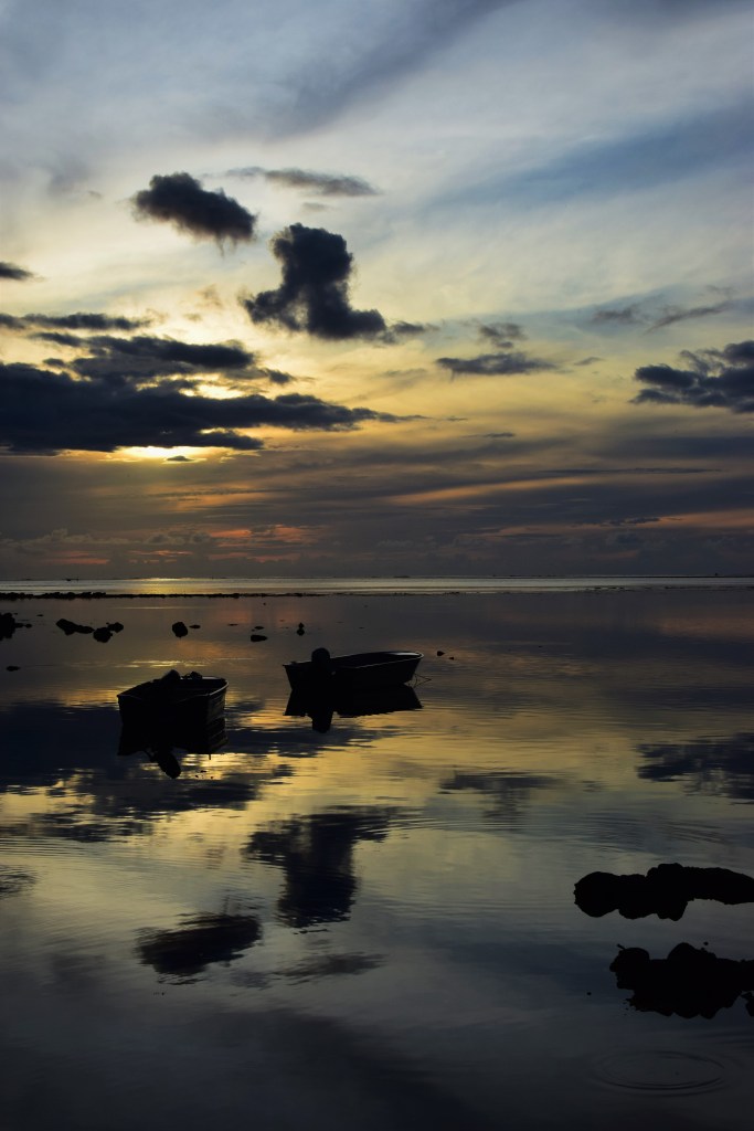 A sunset is reflected on still water with clouds creating contrast and texture. 
