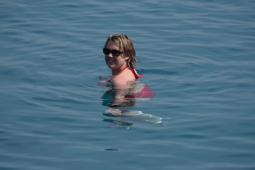 A blond woman in a red bikini is upright in the water looking back at the camera.