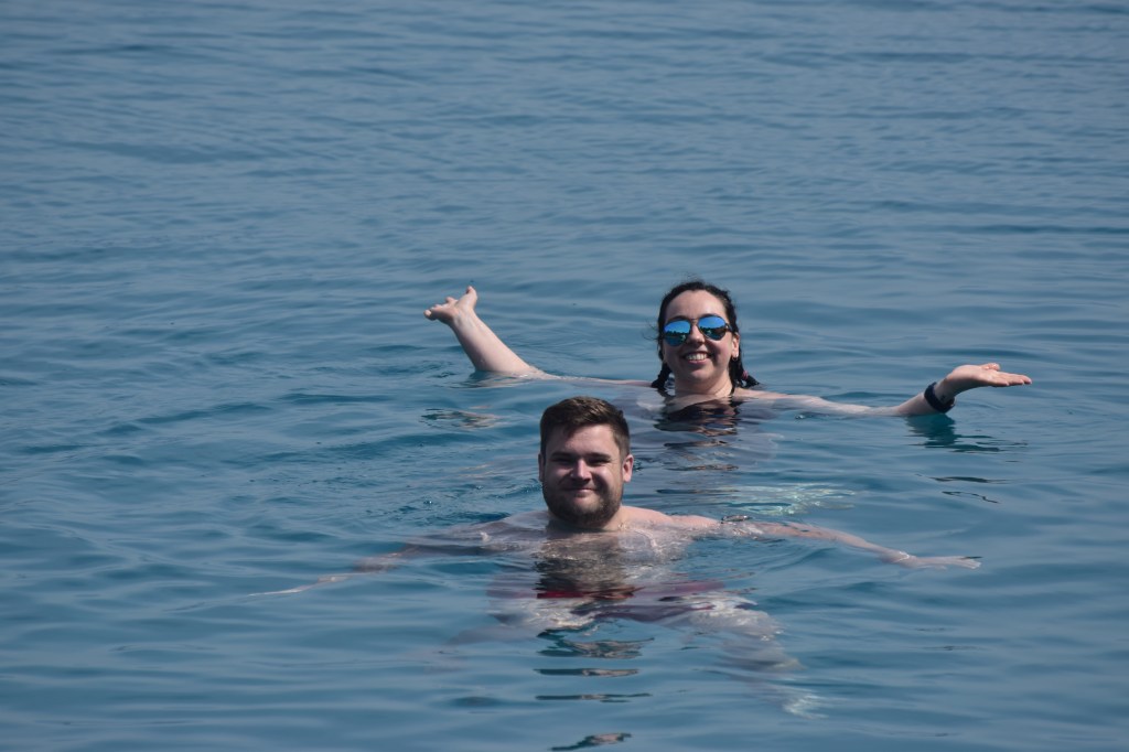 A man and a brunette woman are swimming. The woman is arms up out the water to each side.