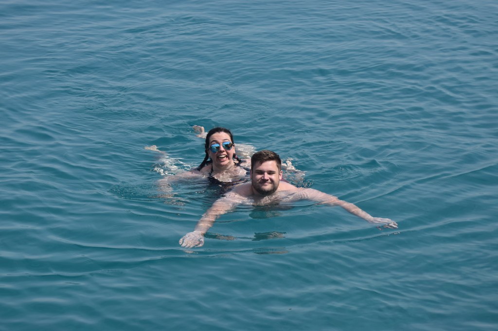 A brunette woman is swimming behind and almost on top of a man