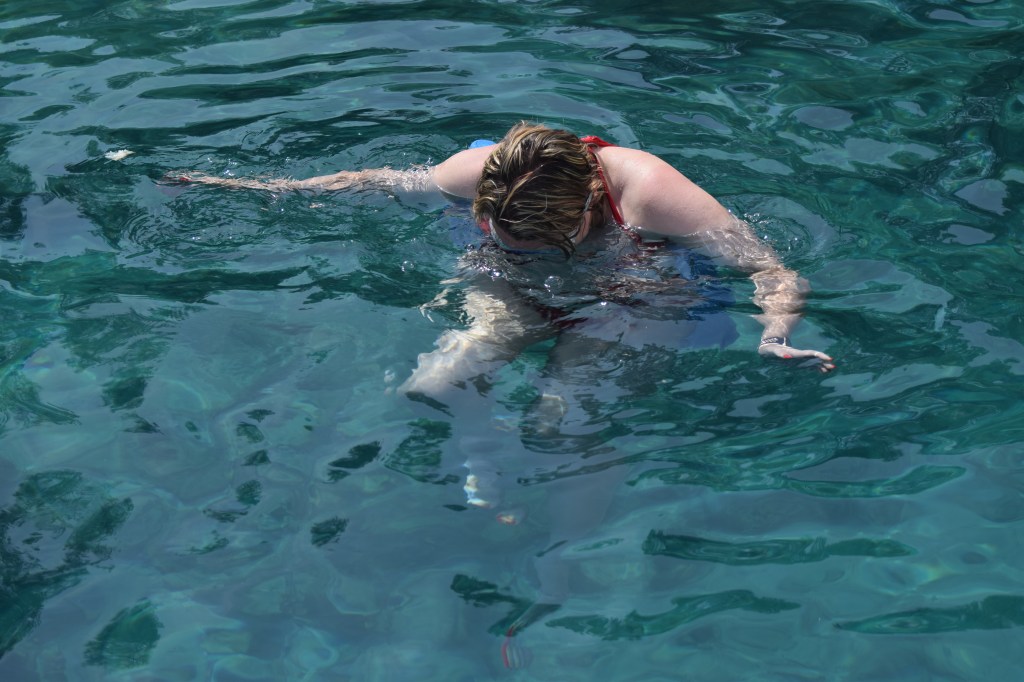 A blond woman is in water looking under the surface.