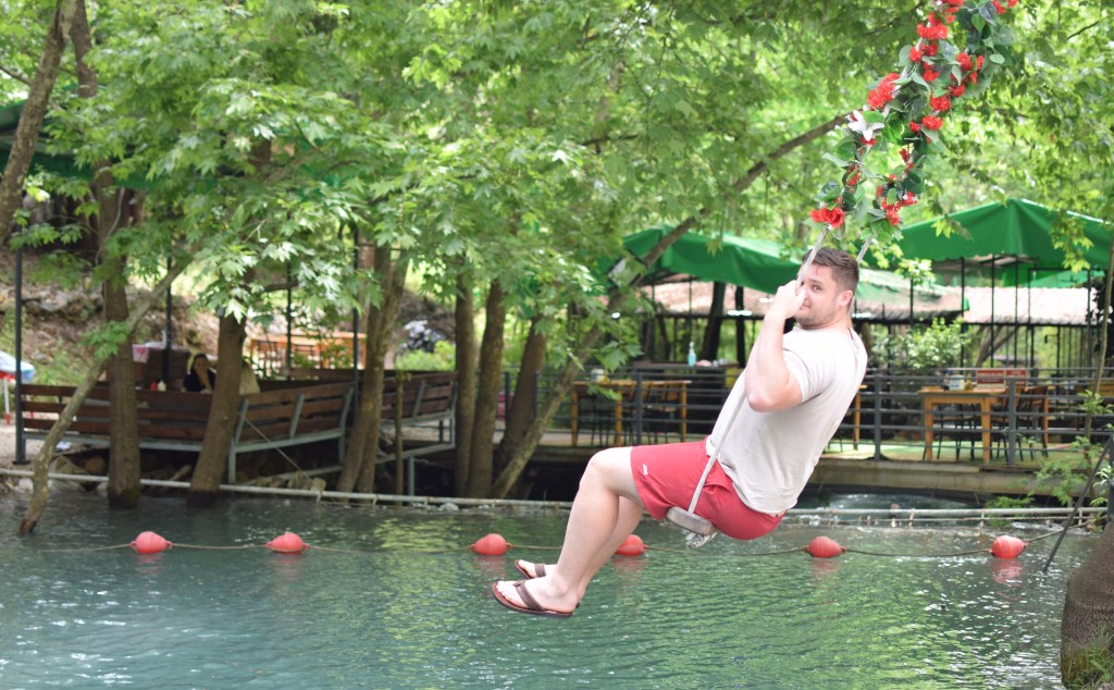 A man is pictured from the side swinging over a river.