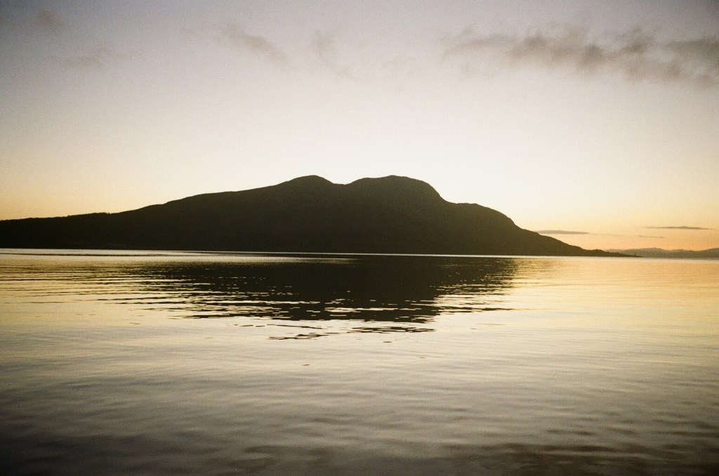 A sunrise image of still water shows a reflection of a silhouetted island.