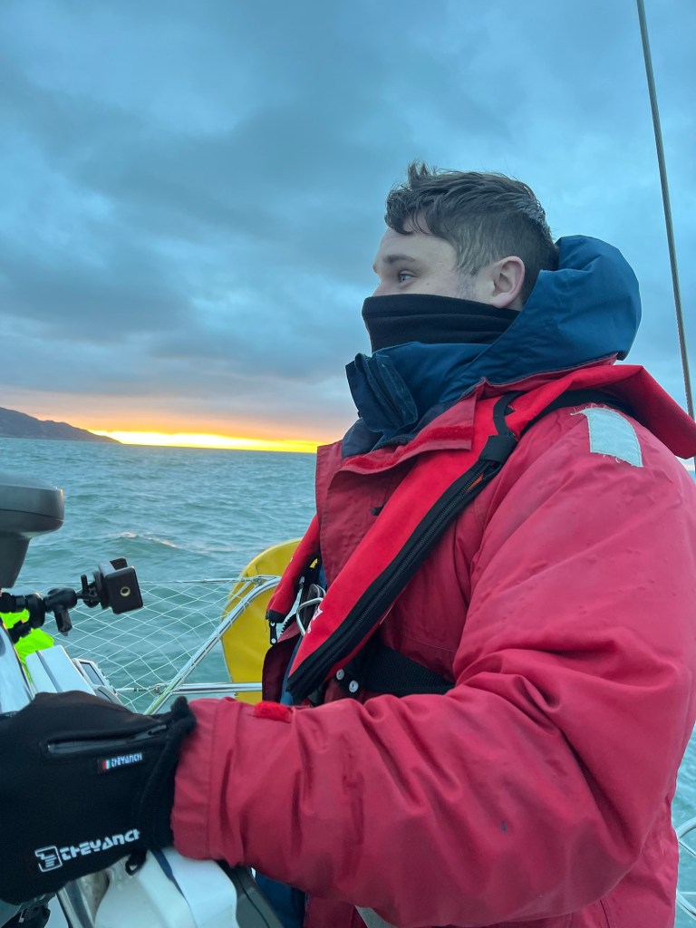 A man wrapped up in obviously many layers is in the foreground with a sunset behind him. 