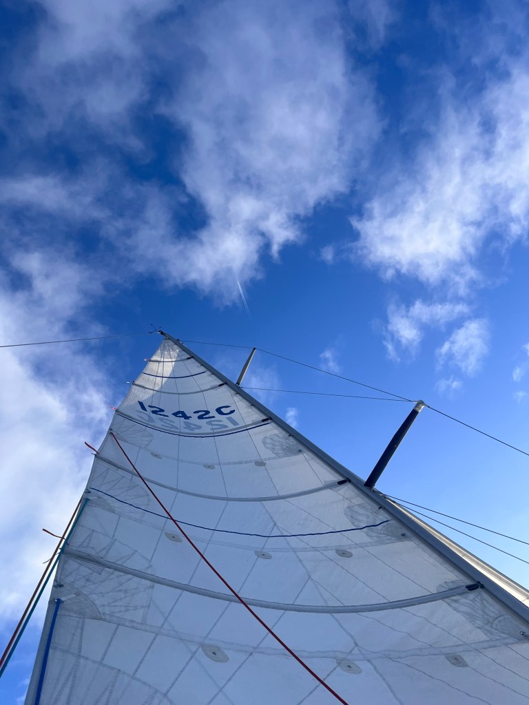 A picture shows the main sail full and a blue sky with scant clouds above. 