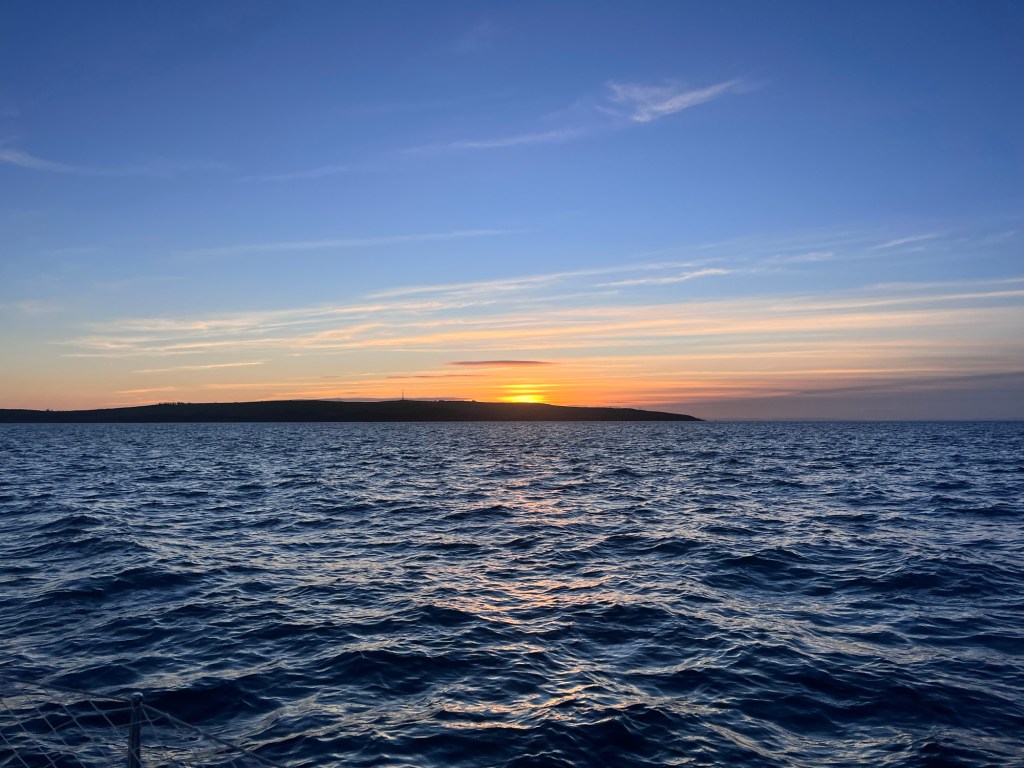 Sunset of a silhouette of land and there is a little chop in the sea. 